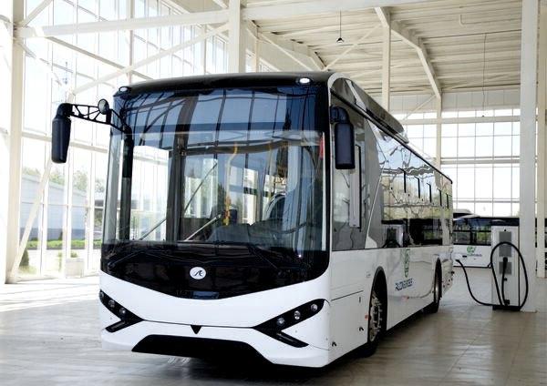 White electric city bus connected to a charging point inside a bright depot facility