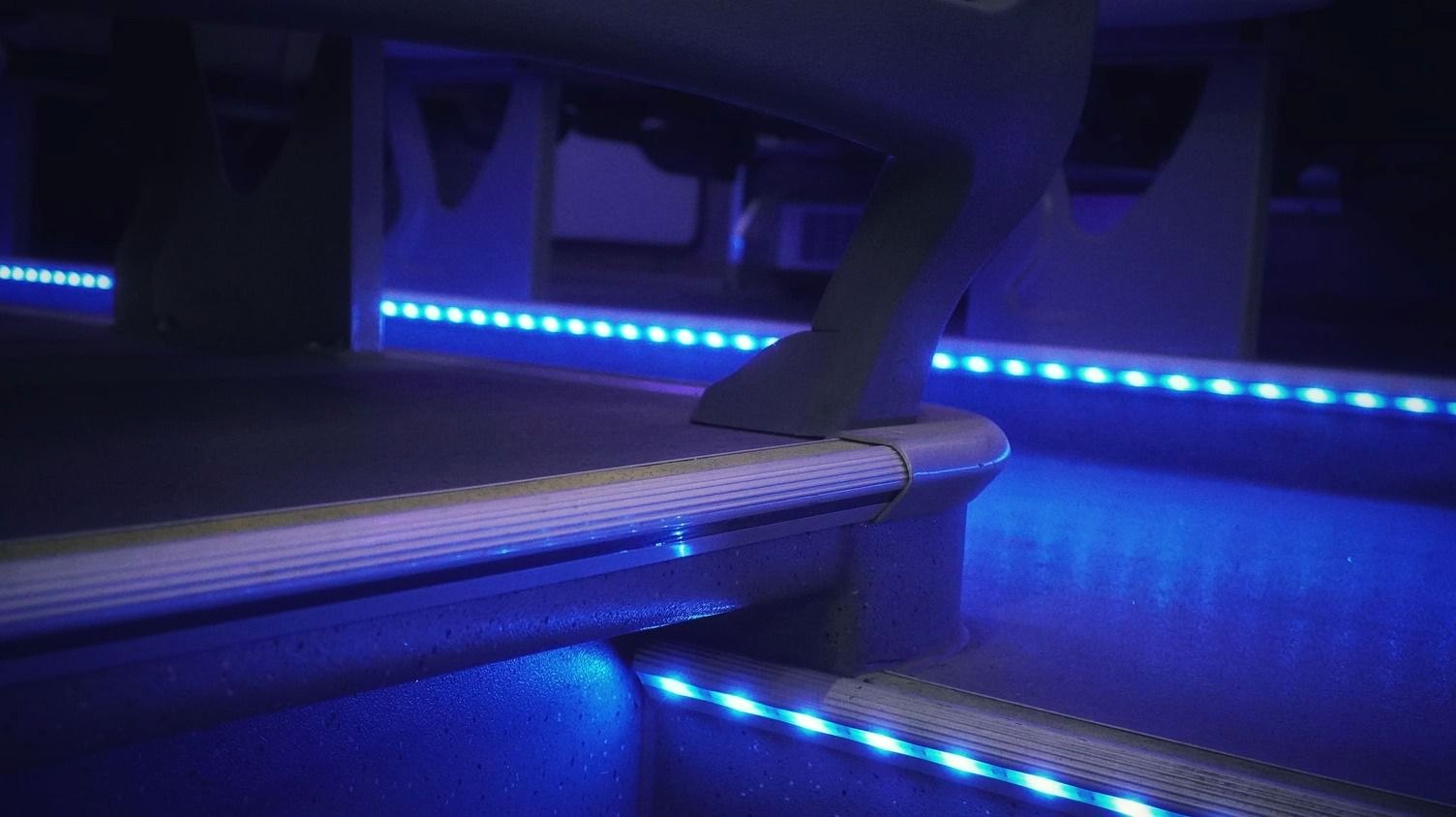 Darkened bus interior lit by blue ambient LED step and aisle lighting