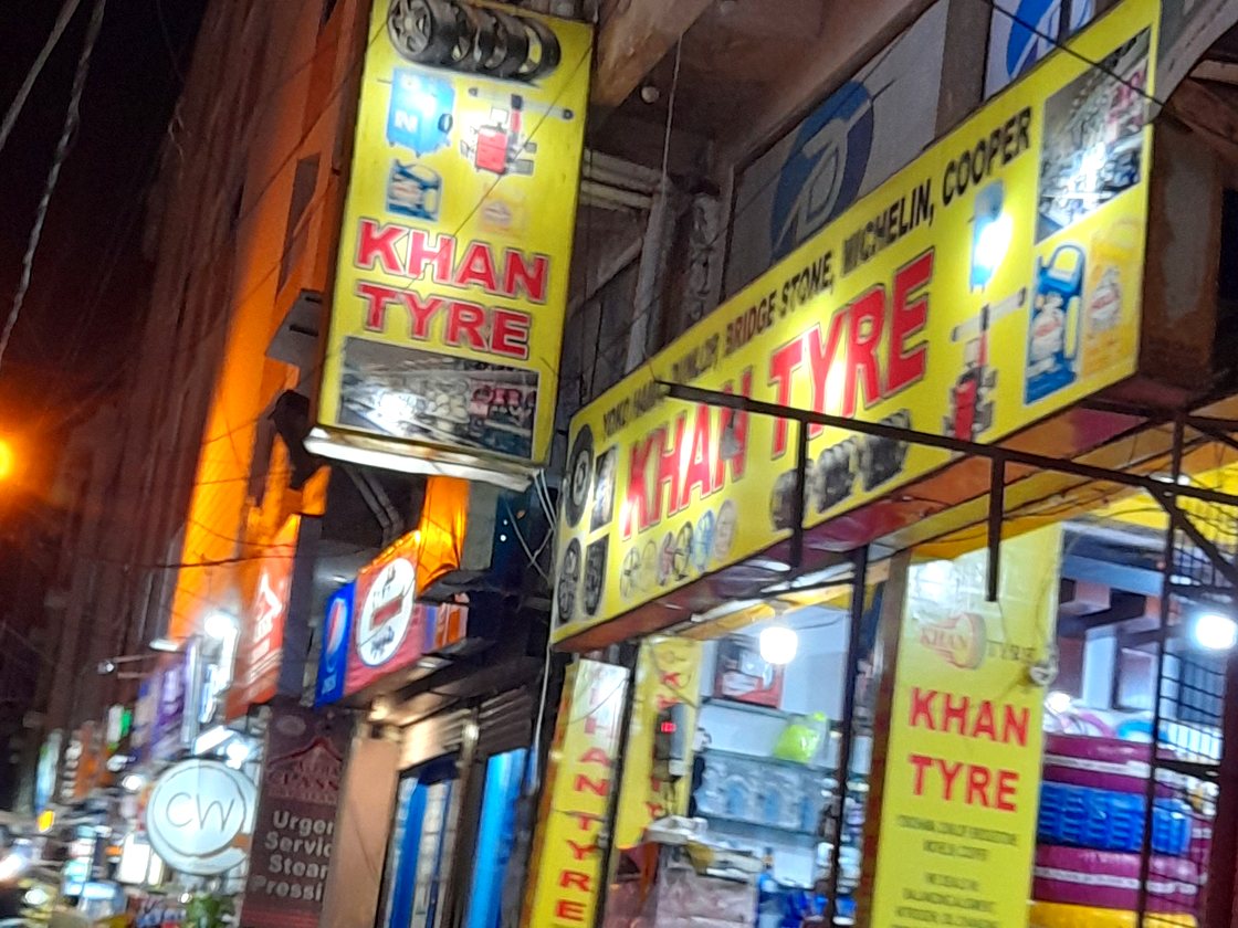 Khan Tyre ka lit-up yellow board raat ko — Badar Commercial, DHA Phase 5 Karachi, tyres aur alloy rims display par